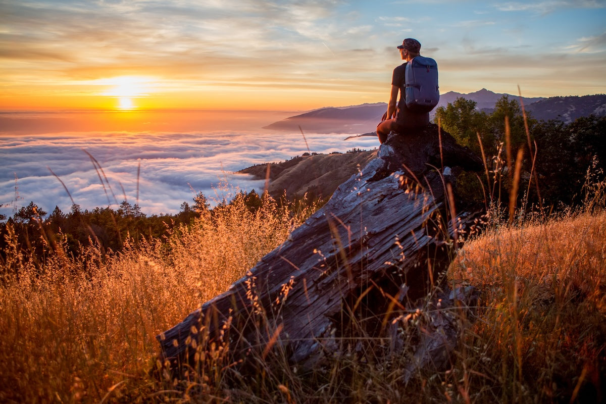 Big Sur woman w backpack w mountains clouds AdobeStock 556783453 compressed
