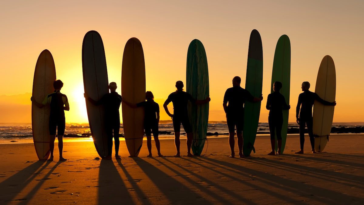 Surfers on beach at sunset iStock 171252100 crop